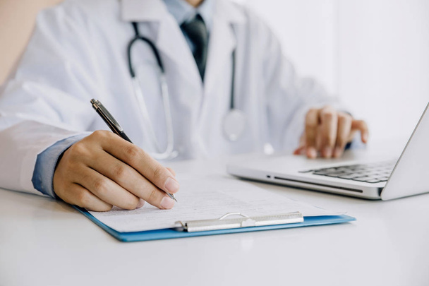 Médico preenchendo formulário médico enquanto sentado na mesa em hosp
 - Foto, Imagem