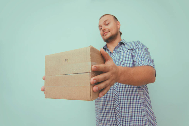 Delivery man with brown box on your home door. Light blue background. Hands hold parcel. Delivery service.  - Foto, Bild