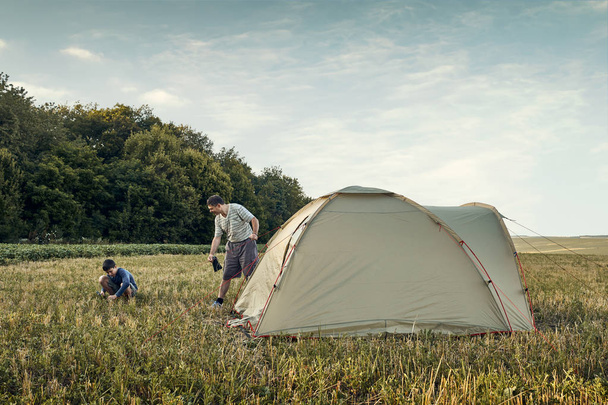 Family set up tent camp at sunset, beautiful summer landscape. Tourism, hiking and traveling in nature. - Photo, Image