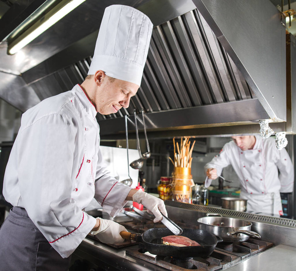 Chef in restaurant kitchen at stove with pan, cooking - Photo, Image