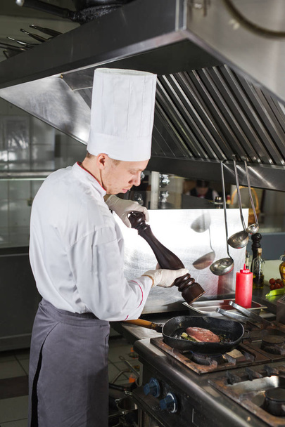 Chef in restaurant kitchen at stove with pan, cooking - 写真・画像