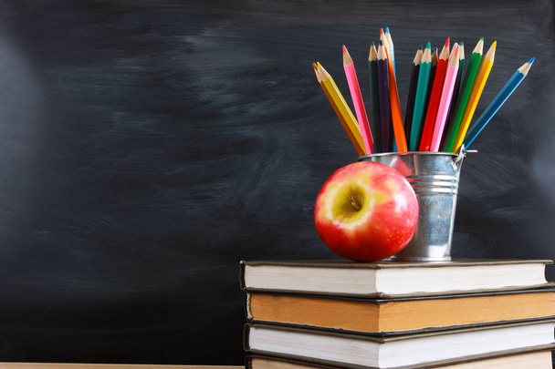 Red apple and colored pencils on stacked books. Classroom blackboard with copy space in background. Education, back to school concept - Foto, Imagem