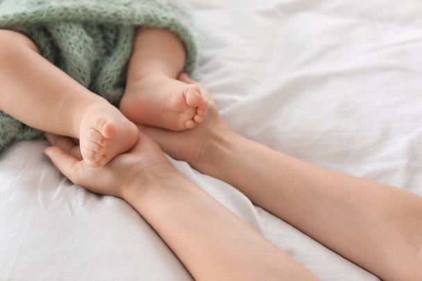 Mother holding feet of her little baby on bed, closeup - Fotoğraf, Görsel