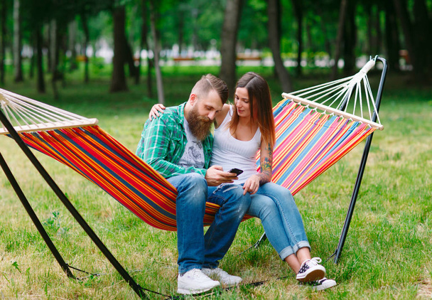Young couple with mobile phone sitting on hammock. - Photo, image