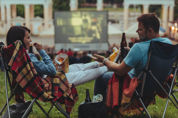 pareja sentada en sillas de campamento en el parque de la ciudad mirando la película al aire libre en el cine al aire libre
 - Foto, imagen
