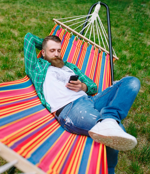 man using an app on his mobile phone white swinging in a hammock. - Photo, Image