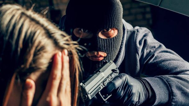 Silahlı maskeli bir soyguncu arabadaki bir kadını tehdit ediyor. Soyguncu - Fotoğraf, Görsel