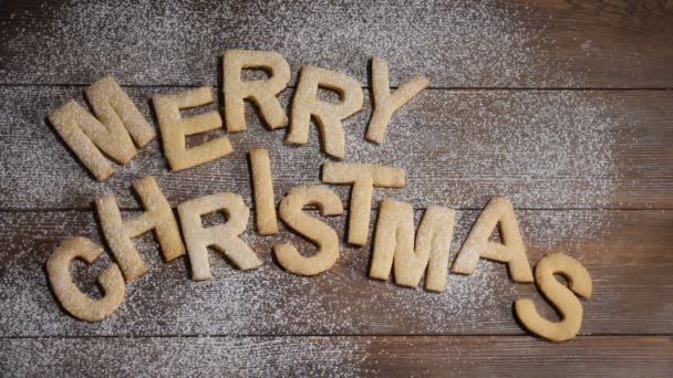 Frohes neues Jahr Konzept. Frohe Weihnachten Notiz mit Keksen Buchstaben auf braunem Holzgrund geschrieben. weißes Pulver fällt in Zeitlupe herunter. hd - Filmmaterial, Video