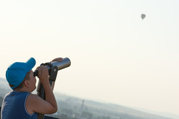 Мальчик смотрит на летающий шар через телескоп
. - Фото, изображение