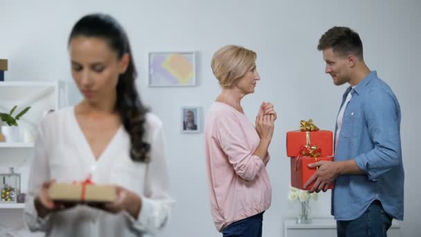 Woman looking at small gift box, while husband giving mother big presents - Záběry, video