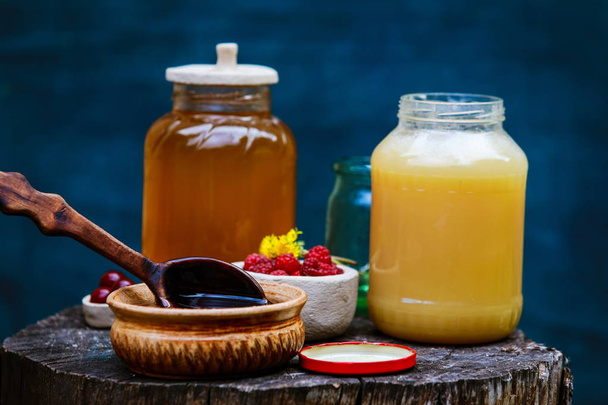 verse zoete honing druipend in een houten lepel in een keramische kom - Foto, afbeelding