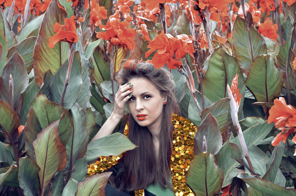 Fashion portrait of caucasian young woman wearing golden jacket posing in red flowers. Glamour festive look. Art collage. Golden glitter tinsel sparkles creative pop art - Fotó, kép
