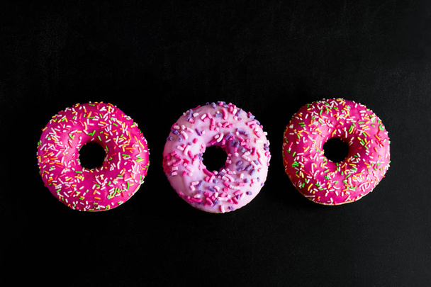 top view pink berry doughnuts row on a black background - Foto, Imagen