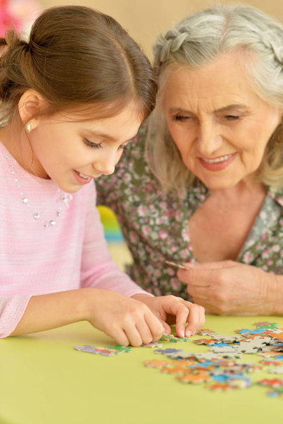 Cute little granddaughter and grandmother collecting puzzles together at home - Photo, Image