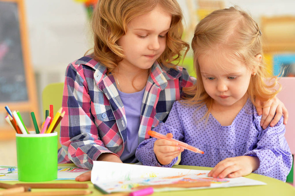 Cute little girls sitting at table and drawing with pencils in their room - Photo, Image