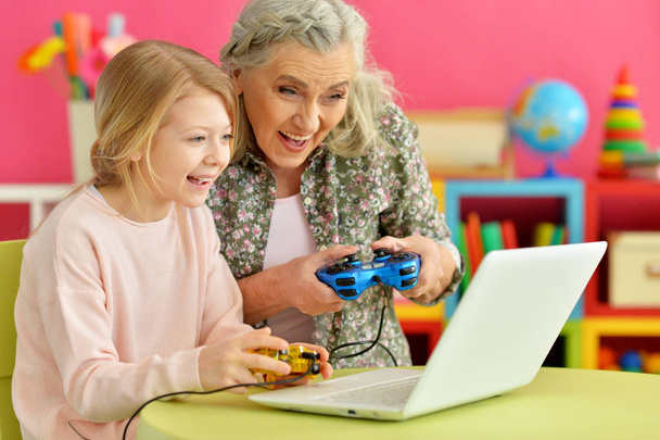 granny with her granddaughter playing computer game on laptop at home - Foto, Imagem
