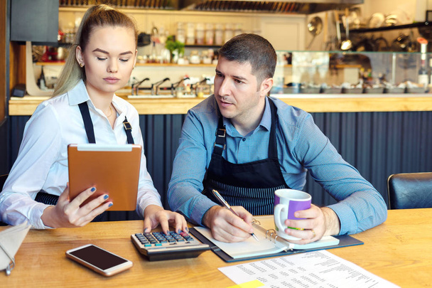 Владельцы небольших семейных ресторанов обсуждают финансы, рассчитывающие счета и расходы нового малого бизнеса - стрессовые мужчины и женщины вместе занимаются бумажной работой в кофейне
 - Фото, изображение