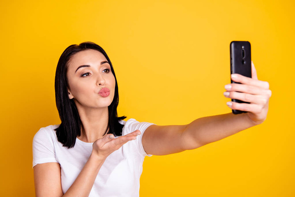 Close up photo beautiful amazing she her lady telephone hand arm make take selfies send air kiss speak talk tell skype boyfriend wear casual white t-shirt jeans denim isolated bright yellow background - Foto, afbeelding