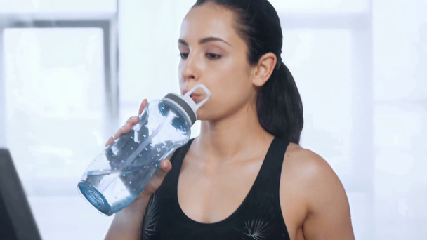 mooie Sportvrouw wandelen op loopband, kijken naar camera en drinkwater in de sportschool - Video