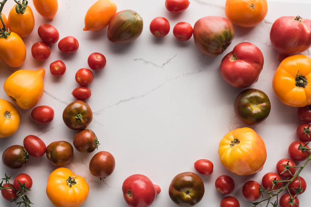 top view of scattered tomatoes with empty space in middle on marble surface  - Photo, Image