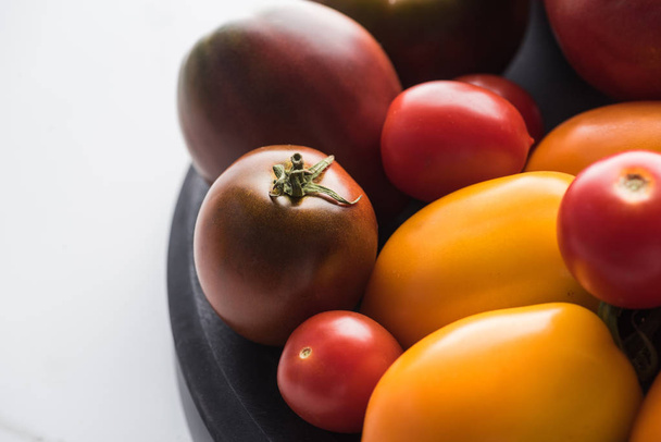 close up view of red and yellow tomatoes on wooden pizza pan on marble surface  - Foto, immagini