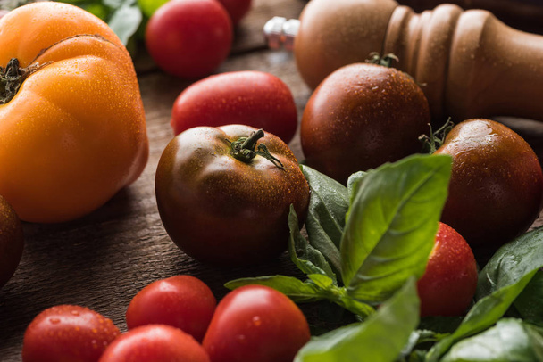 close up view of tomatoes with spinach near salt mill on wooden surface  - Foto, Bild