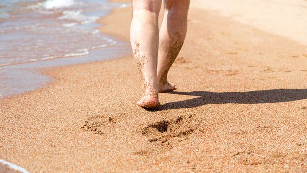 Primer plano de los pies desnudos en la playa. Caminando sobre la arena en el borde del agua. Concepto de vacaciones y viajes. Pies de hombre. Viaje a la playa piernas masculinas en la playa de arena
 - Foto, imagen