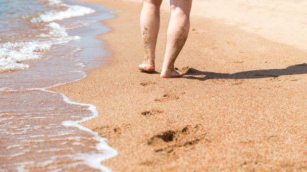 ビーチで素足のクローズアップ。水辺の砂の上を歩く休暇と旅行の概念。男性の足。ビーチ旅行 - 砂浜の男性の足 - 写真・画像