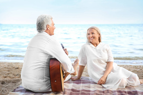 Mature man playing guitar for his wife at sea resort - Photo, Image