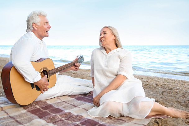 Mature man playing guitar for his wife at sea resort - 写真・画像