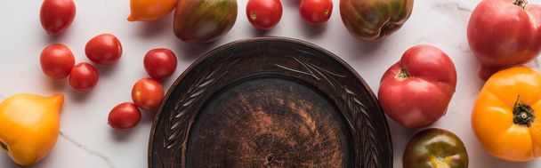 panoramic shot of empty wooden plate near scattered tomatoes on white marble surface  - Photo, Image