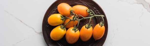 panoramic shot of yellow tomatoes on wooden plate on marble surface  - Fotó, kép