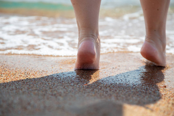 Nahaufnahme von nackten Füßen am Strand. Wandern auf dem Sand am Rande des Wassers. Urlaubs- und Reisekonzept. Frauenbeine. Kosmetik und Körperpflege. Strandreise - Frauenbeine am Sandstrand - Foto, Bild