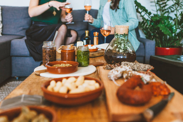 kaksi nuorta naista ystävät rentoutuvat yhdessä istuu sohvalla viiniä ja tapaksia ruokaa
 - Valokuva, kuva