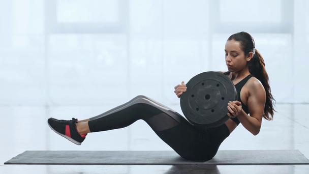 schöne Sportlerin beim Bauchmuskeltraining mit Hantelscheibe auf Fitnessmatte im Fitnessstudio - Filmmaterial, Video