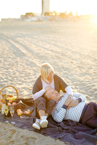 Ηλιοφάνεια φωτογραφία του ανώτερου συζύγου που βρίσκεται στη γυναίκα γόνατα και καρό, σαμπάνια και φρούτα. - Φωτογραφία, εικόνα