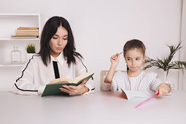 Pretty mother with cute daughter sitting with book in the room at home. - Φωτογραφία, εικόνα