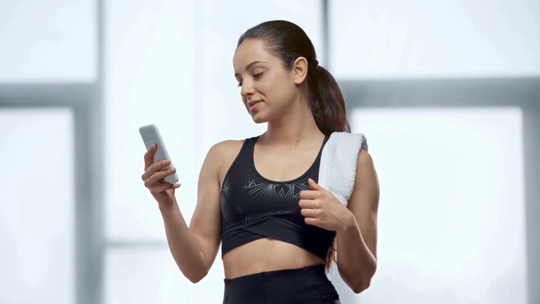 hermosa joven deportista con toalla usando teléfono inteligente en el gimnasio
 - Metraje, vídeo