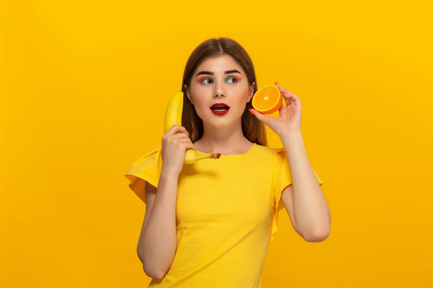 junges Model in gelbem T-Shirt hält Banane und Orange vor gelbem Hintergrund. - Foto, Bild