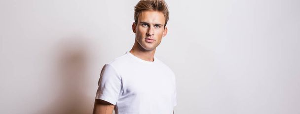 Elegant young handsome man in white T-shirt. Studio portrait. - Valokuva, kuva