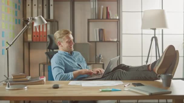 Handsome Young Entrepreneur Works on a Laptop with His Legs Up on the Desk. Designer Uses Notebook to Create Software Unicorn Startup. Chill Student Writing Paper for University - Felvétel, videó