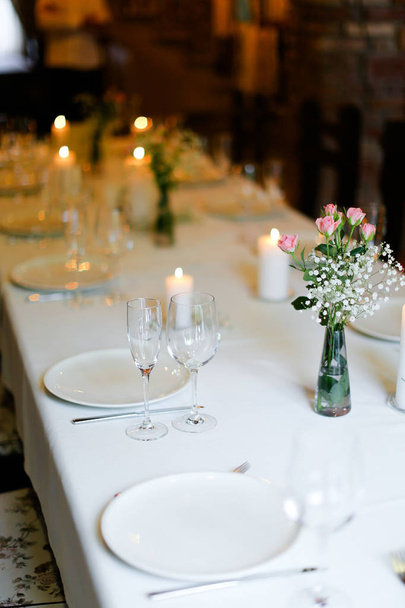 Μπουκέτο λουλούδια, λευκές πλάκες και πιρούνια, κεριά στο τραπέζι. - Φωτογραφία, εικόνα