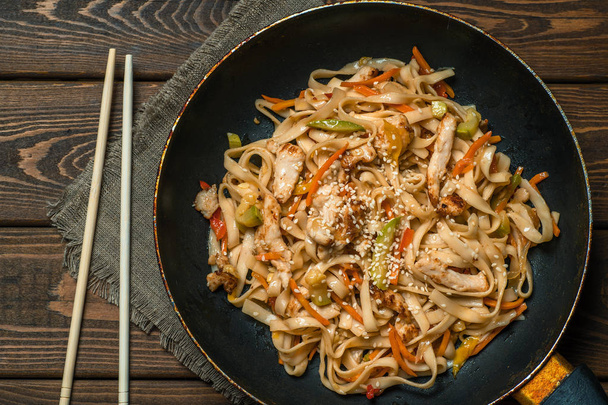 Fry noodle-ahşap masa üzerinde kızarmış tavuk ve sebze ile geleneksel Çin Wok, üst görünüm - Fotoğraf, Görsel