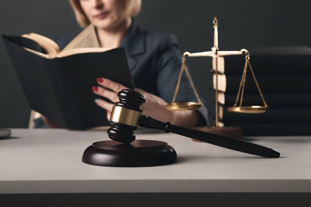 Woman lawyer reading professional books in office. Wooden gavel and libra on the desk. - Photo, Image