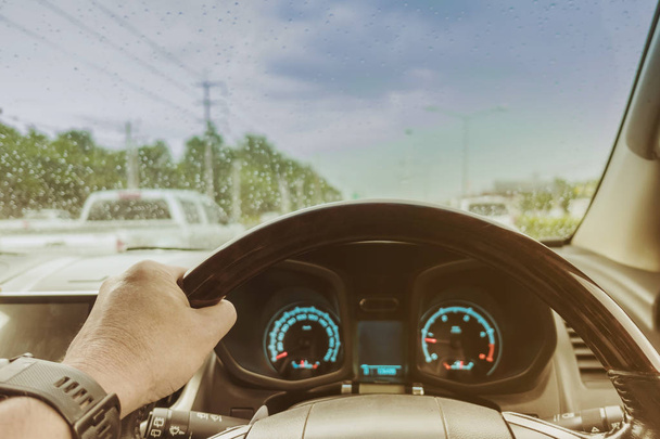 Одна рука водія на кермі автомобіля зі швидкістю і дощем на вітровому склі в дощовий день
. - Фото, зображення