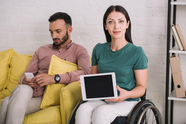 attractive disabled woman showing digital tablet with blank screen while sitting near boyfriend using smartphone - Foto, imagen