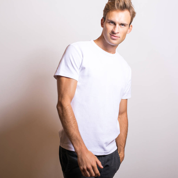 Elegante joven guapo hombre en camiseta blanca. Retrato de estudio
. - Foto, imagen