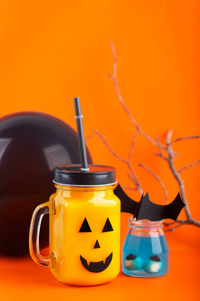 Halloween healthy pumpkin or carrot drink in the glass jar with scary face on a orange background - Фото, изображение
