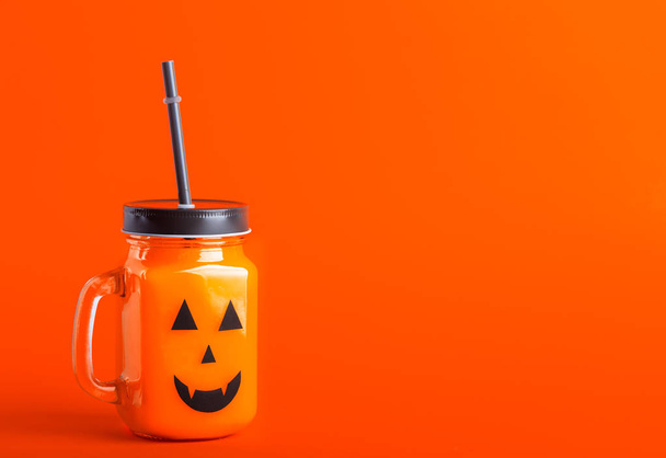 Halloween healthy pumpkin or carrot drink in the glass jar with scary face on a orange background - Photo, Image