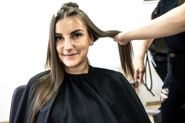 Schattig meisje met lange brunette haarkapper doet haar lamineren in een schoonheidssalon. concept van haarverzorgings behandeling - Foto, afbeelding